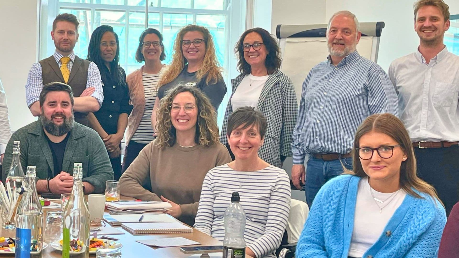 Training participants and facilitators during a workshop, seated and standing around a table.